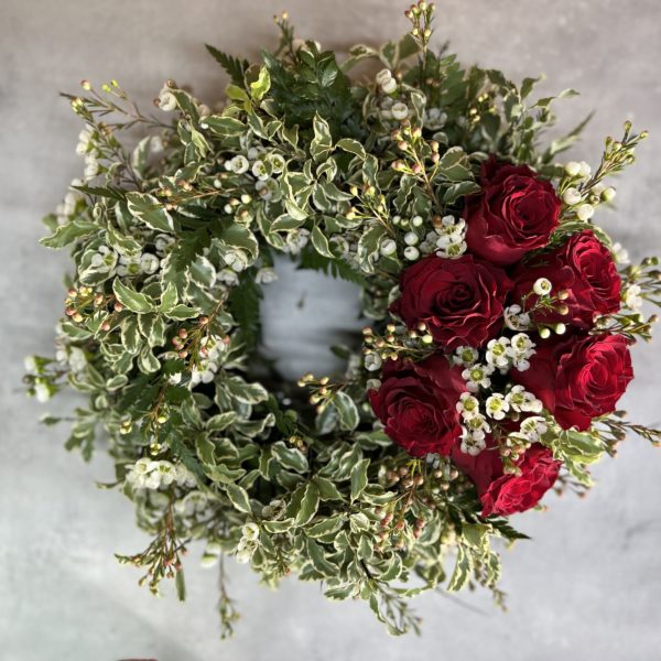 A photograph of a funeral and sympathy wreath with a solection of foliages and bright red roses.