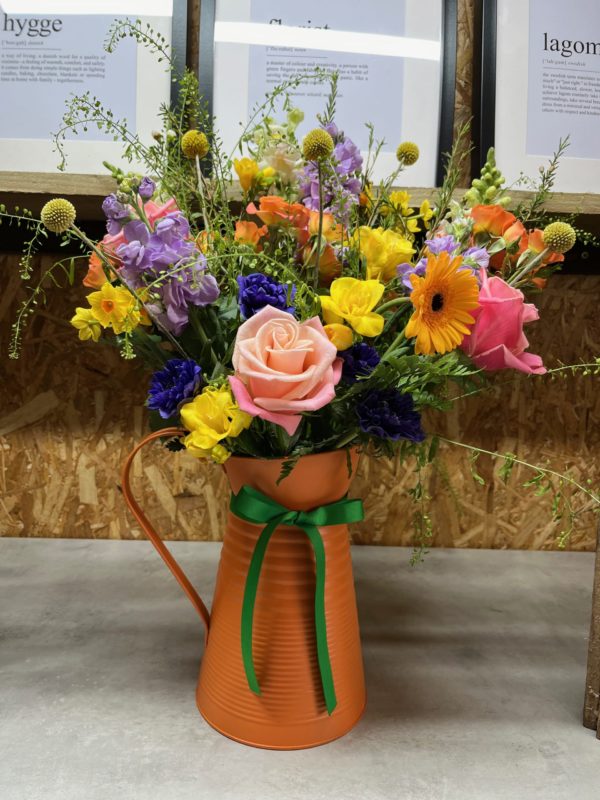 Photograph of a vibrant tin flower jug filled with colourful flowers and an equally vibrant ribbon. Designed by Hygge Flower Studio, Langford Budville Somerset. Order online