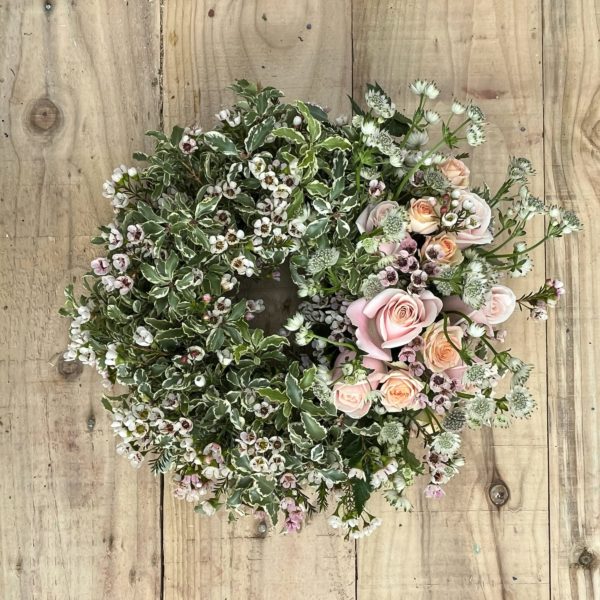 A photograph of a funeral and sympathy wreath with countryside foliage and beautiful pink and peach roses, astrantia and waxflower