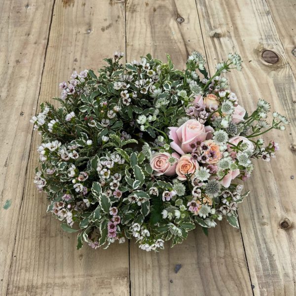 A tilted photograph of a funeral and sympathy wreath with countryside foliage and beautiful pink and peach roses, astrantia and waxflower